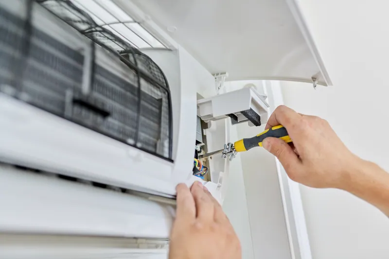 Manos de un técnico ajustando una unidad interior de aire acondicionado