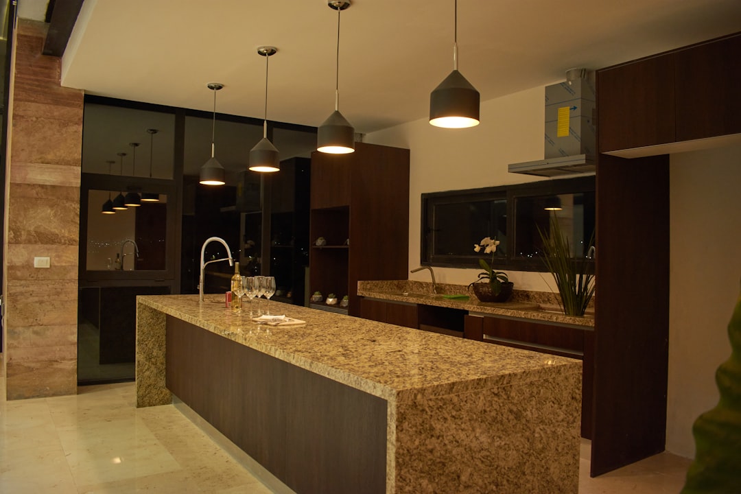 Cocina abierta con isla de granito y salón integrado, un proyecto de reforma de Reformatta en Barcelona
